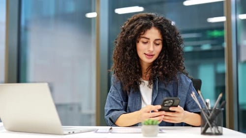 Young Businesswoman Using Laptop and Smartphone in Modern Office