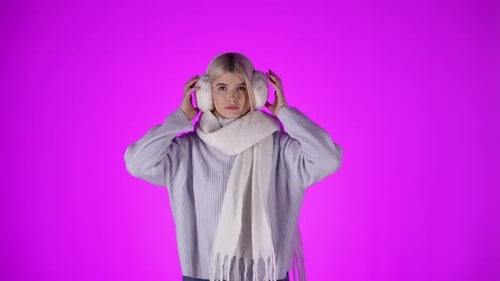 Caucasian woman with scarf takes off fluffy white ear warmers, studio shot