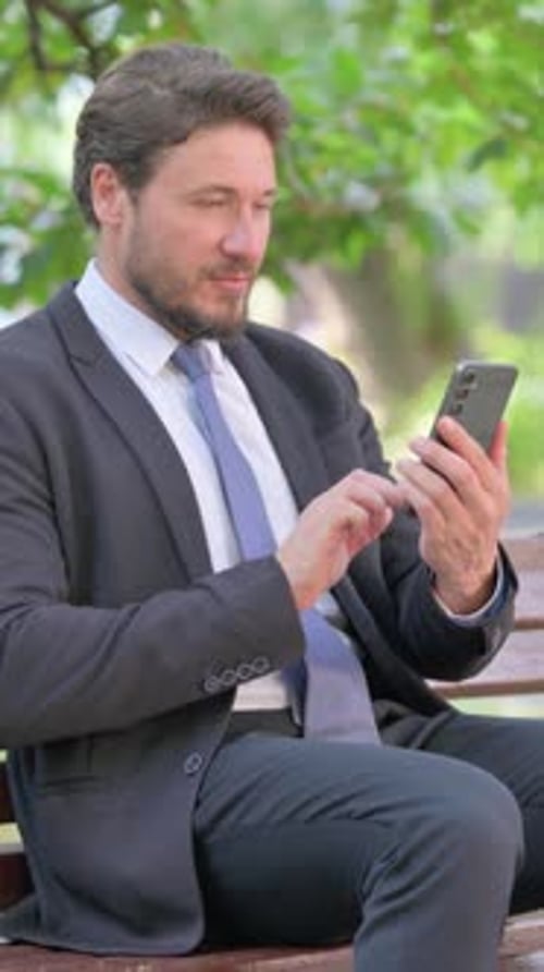 Man in suit sits on bench using phone