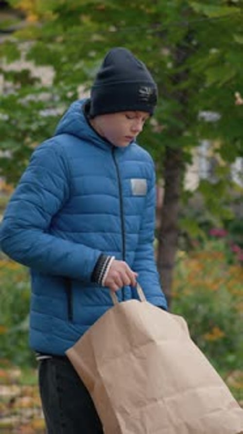 Boy Dumping Brown Leaves from Bag in Park