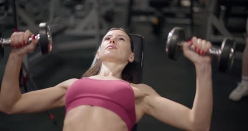 A Young Beautiful Brunette Girl in Sportswear is Exercising on a Machine in the Gym Doing Arm