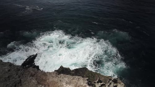 Steady, high angle view of wild white waves splashing onto rocky island shore