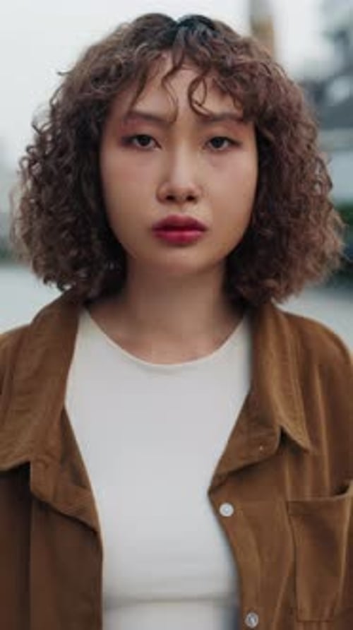 Vertikales Videoporträt eines seriösen jungen chinesischen Mädchens im Teenageralter mit Piercings und lockigem Haar