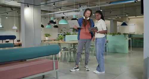 Des collègues africains repérent les détails d'un ordinateur portable, pointent du doigt et tapotent une tablette tout en travaillant dans le salon
