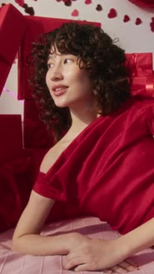 Vertical Portrait of Gen Z Girl on Bed with Red Present Boxes Stacked Behind