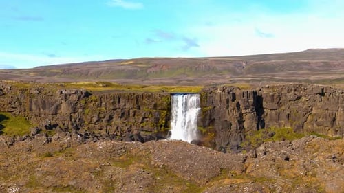 Drone aérien filmé au-dessus d'une grande plaine islandaise avec une grande cascade traversant une faille sur la