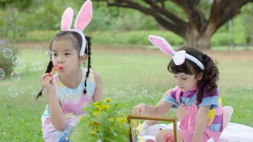 Happy two little asian girl wear bunny ears blowing soap bubbles playing alone in the park