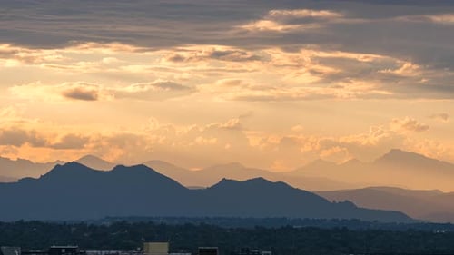 Sunset motion time lapse as golden clouds move over Rocky Mountain Range, Denver