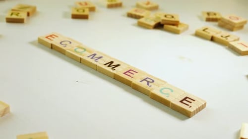 Someone writing Ecommerce with wooden tiles letters. Off white background. Flat plane. Dutch angle