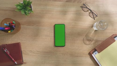 Top down view of a mock up green screen smartphone on a wooden desk