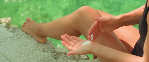 Legs and hands with lotion. Woman applying sunscreen on body at the beach. Self-care routine during