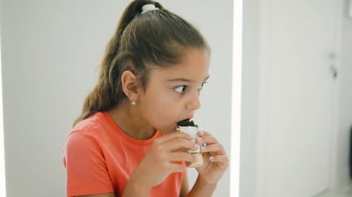 A Young Girl Delightfully Savoring a Tasty Snack in a Bright and Modern Indoor Space Surrounded By