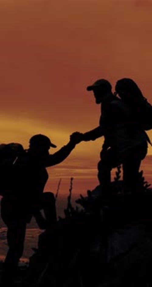 People, silhouette and helping hand for hiking on mountain at sunset, friends