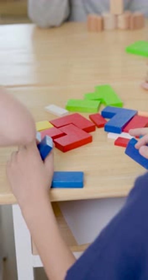 Vertical close view follows young pupil hands arranging colorful block pieces on classroom table,