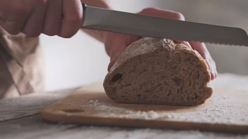 Person Slicing Fresh Bread Loaf on Wood Board