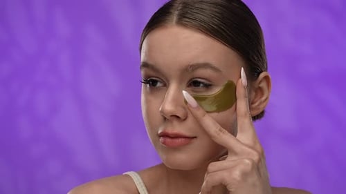 Young Woman with Makeup Posing at Camera in Studio Smiling Applying Eye Patch Under Eye Close Up