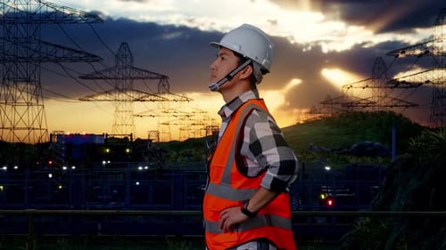 Side View Of Asian Male Engineer Looking Around With Arms Akimbo Near High voltage tower