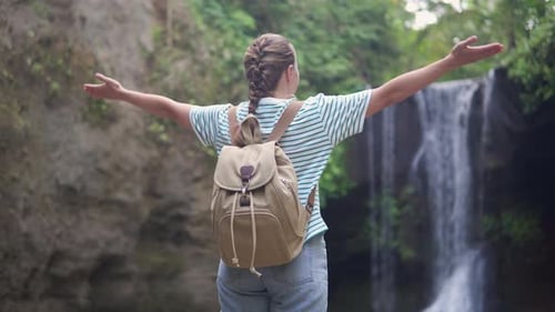 Female tourist with backpack is enjoying view of a waterfall