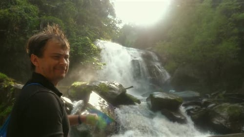 Man Enjoying Nature and Pointing at Beautiful Waterfall in Lush Forest