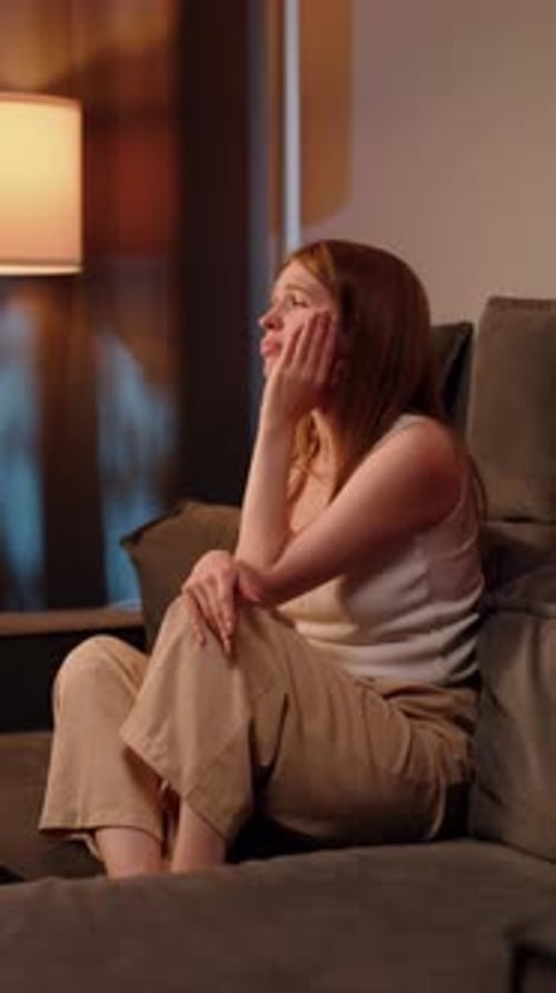 Woman Comforting Herself While Sitting on Sofa at Home in Evening