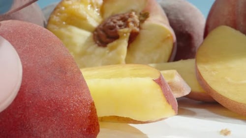 Slicing peaches into pieces, on a white table under the sun and blue sky, super close-up, slow motio