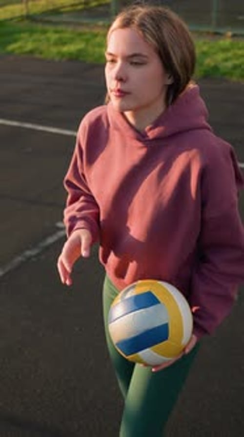 Young Athlete Bouncing Volleyball Preparing to Serve in Outdoor Court with Greenery and Markings