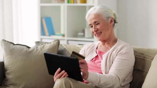 Senior Woman Using Tablet and Credit Card on Sofa
