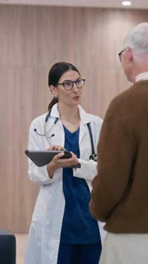 Vertical of General Practitioner with Tablet Consulting Aged Patient in Clinic