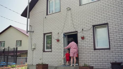 Padre que ayuda al niño pequeño a través de la entrada exterior, mujer vestida de rosa guiando al niño pequeño