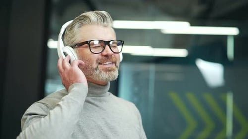 Close up. Happy mature gray haired bearded man in glasses relaxing listening to music with headphone
