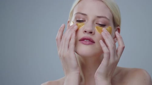 Young Woman Applies Gold Cosmetic Eye Patches