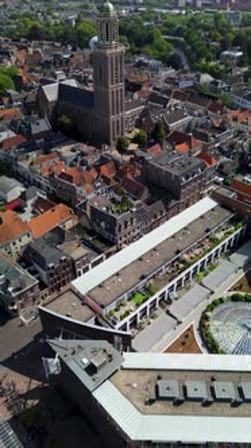 Drone footage shows a historic European city with a tall church tower rising above red-roofed houses