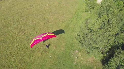 Paraglider takes flight. Man with red parachute runs down slop and begins to sail through the air pa