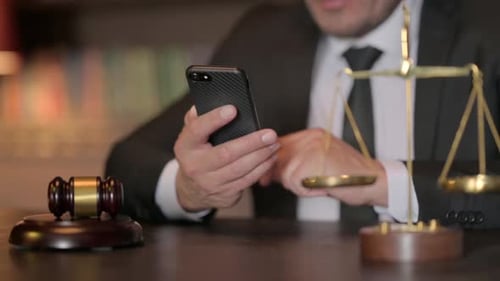 Close up of Judge Browsing Smartphone in Court, Scale of Justice