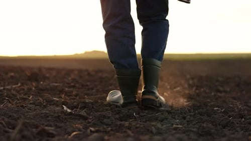 Agriculture. Cropped shot of back view businessman farmer in rubber boots walks along plowed field