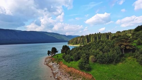 Lake with Clear Water and Stone Shore in Spruce Forest with Fir Trees Against a Daytime Sky