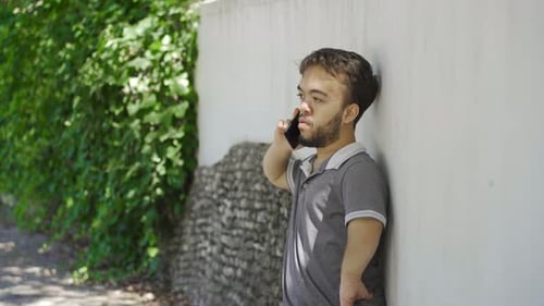 Outdoors dwarf young man arguing with the person he is talking to on the phone.