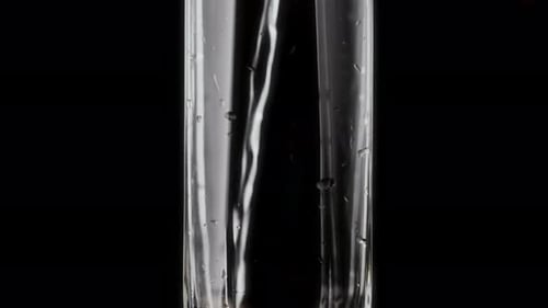 Water is Poured Into a Faceted Glass on a Black Background