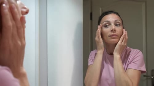 Woman Applying Lotion to Face in Mirror