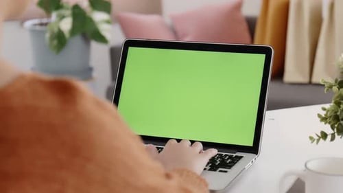 Young Asian woman using laptop computer at home with green blank monitor screen.