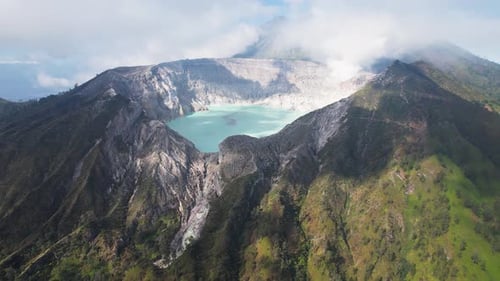 Aerial Circling The Rim Of A Steaming Volcano Ijen with a Turquoise Lake, and foggy cloudy Mountain