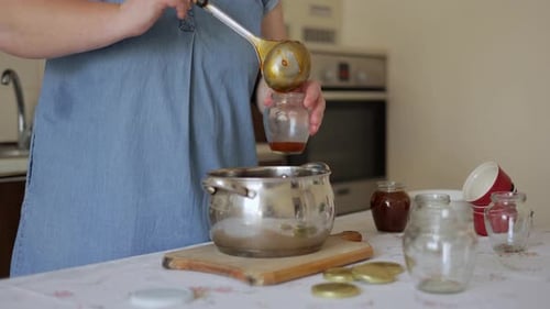 Female hands pour ready-made apricot jam into a glass jar. Homemade apricot jam.