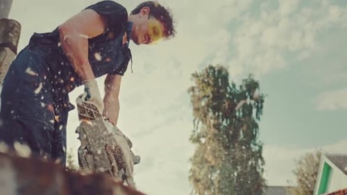 Man Cutting Wood with Chainsaw Outdoors