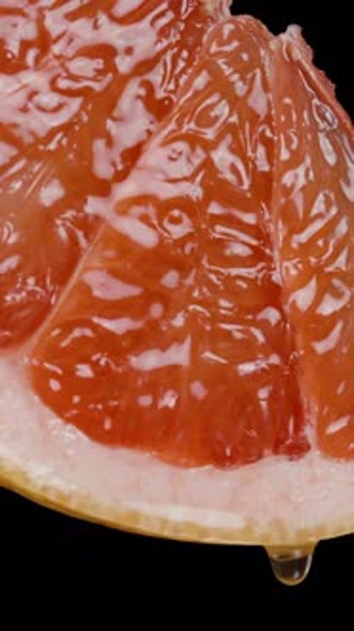 Vertical video. From a slice of grapefruit with red juicy flesh, drops of juice are dripping.