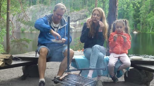 A Couple with a Child Grilling in the Forest on the Shore of the Lake