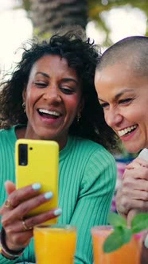 Cheerful Multiethnic Female Friends Enjoying Drinks at a Bar Having Fun Watching Gossip on a Mobile