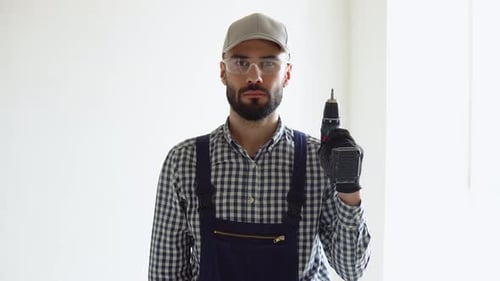 Cheerful Young Man in Coveralls Hold Electric Drill in Office or Apartment