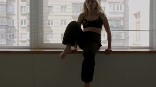 Zeitgenössische Tänzerin übt Bewegungen auf Posen auf der Fensterbank im Studio