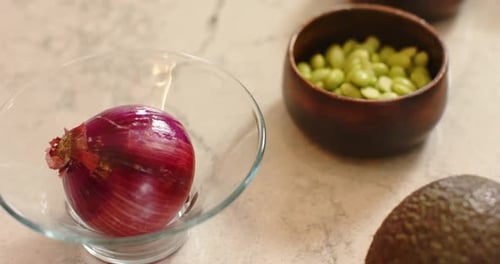 Camera panning shifting red onion left centering bean bowl showing seasoning avocado on countertop