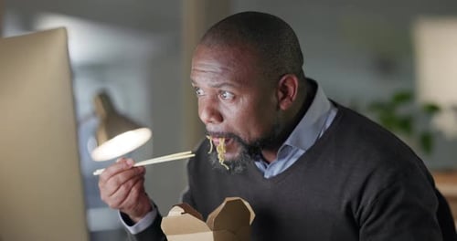 Businessman in office at night, eating fast food at computer and reading email